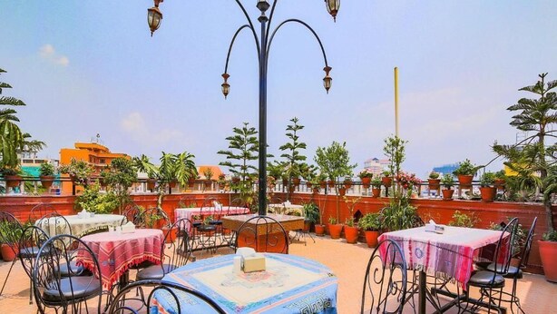 An outdoor terrace with tables and chairs, surrounded by potted plants and a clear sky.