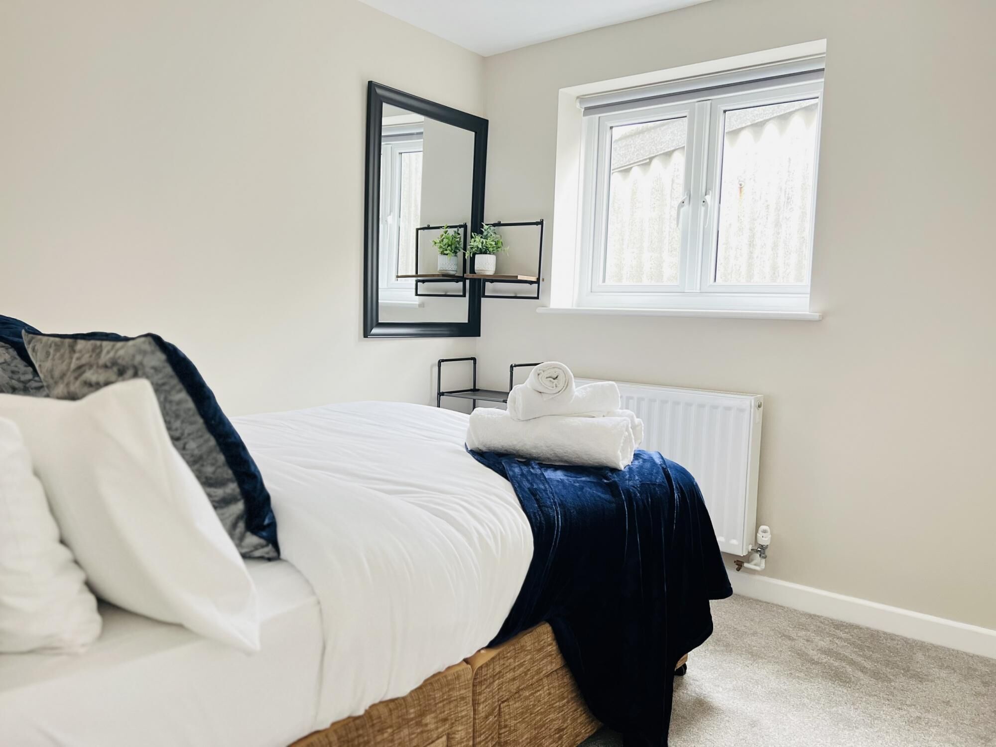 A bedroom with a bed, a window, a radiator, and a mirror.