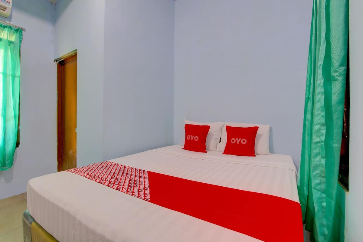 A neatly made bed with a red and white bedspread, two red pillows with the word "OYO" on them, and green curtains on the windows.