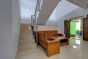 A staircase with a wooden handrail and a wooden bed with intricate designs in a room with white walls and a green screen in the background. - Hotel O Griya Kencana Asri Syariah (Surakarta)