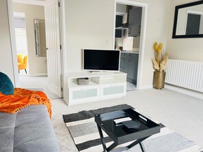 A modern living room with a sofa, a TV on a white cabinet, a black coffee table, and a kitchen in the background. - Amber Apartment 2 in Newmarket (Newmarket)