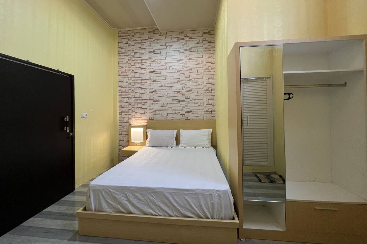Ein Schlafzimmer mit einem Bett, einem Nachttisch mit Lampe, einem Kleiderschrank und einem Spiegel.