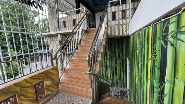 A staircase with wooden steps and metal railings, leading to a balcony with a stone wall and a view of greenery. - Hotel O Batodupi Guesthouse Syariah Near Buttu Kasambi (Makassar)