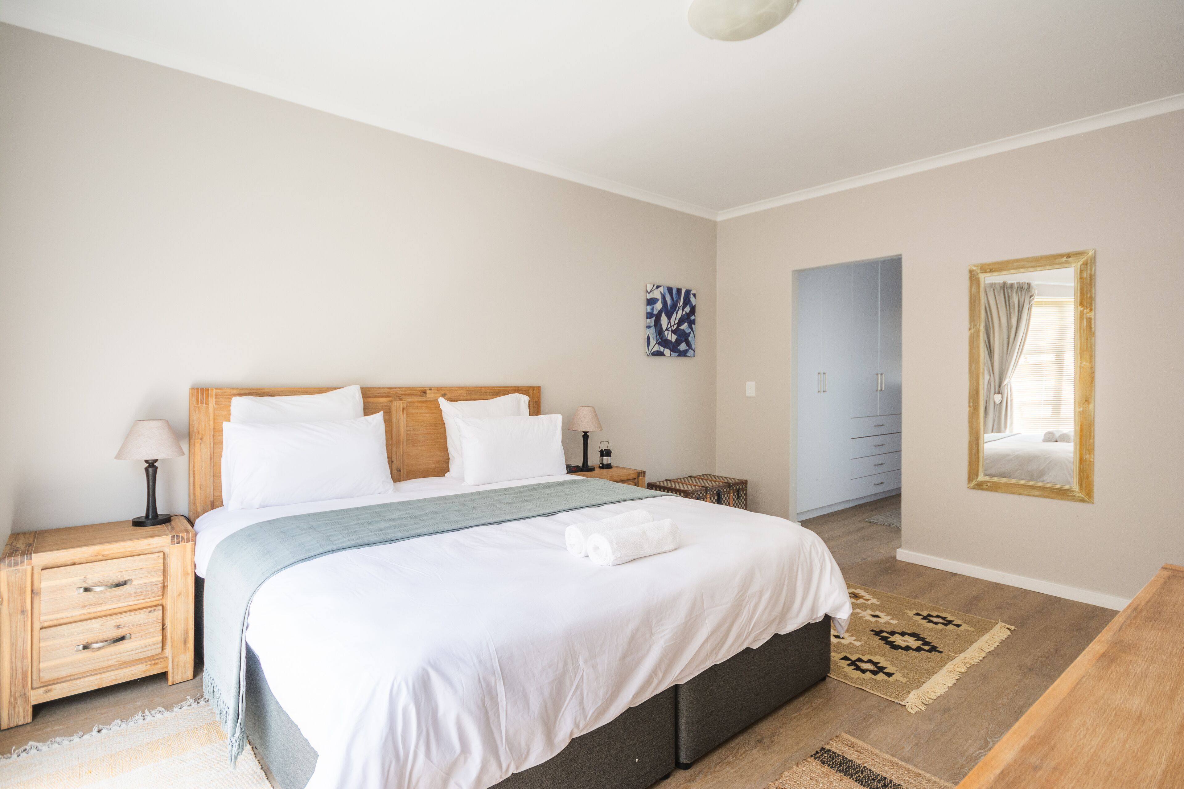 A bedroom with a bed, bedside tables, a lamp, a mirror, and a door leading to another room.