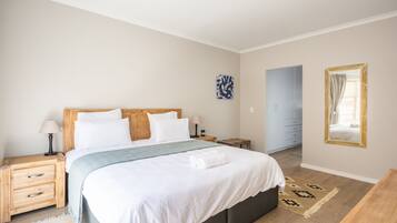A bedroom with a bed, bedside tables, a lamp, a mirror, and a door leading to another room.