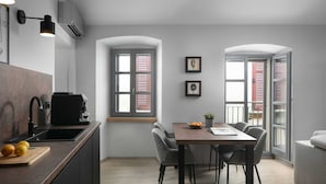 Una cucina moderna con zona pranzo, che include una macchina da caffè, una ciotola di frutta e una pianta in vaso sul tavolo.