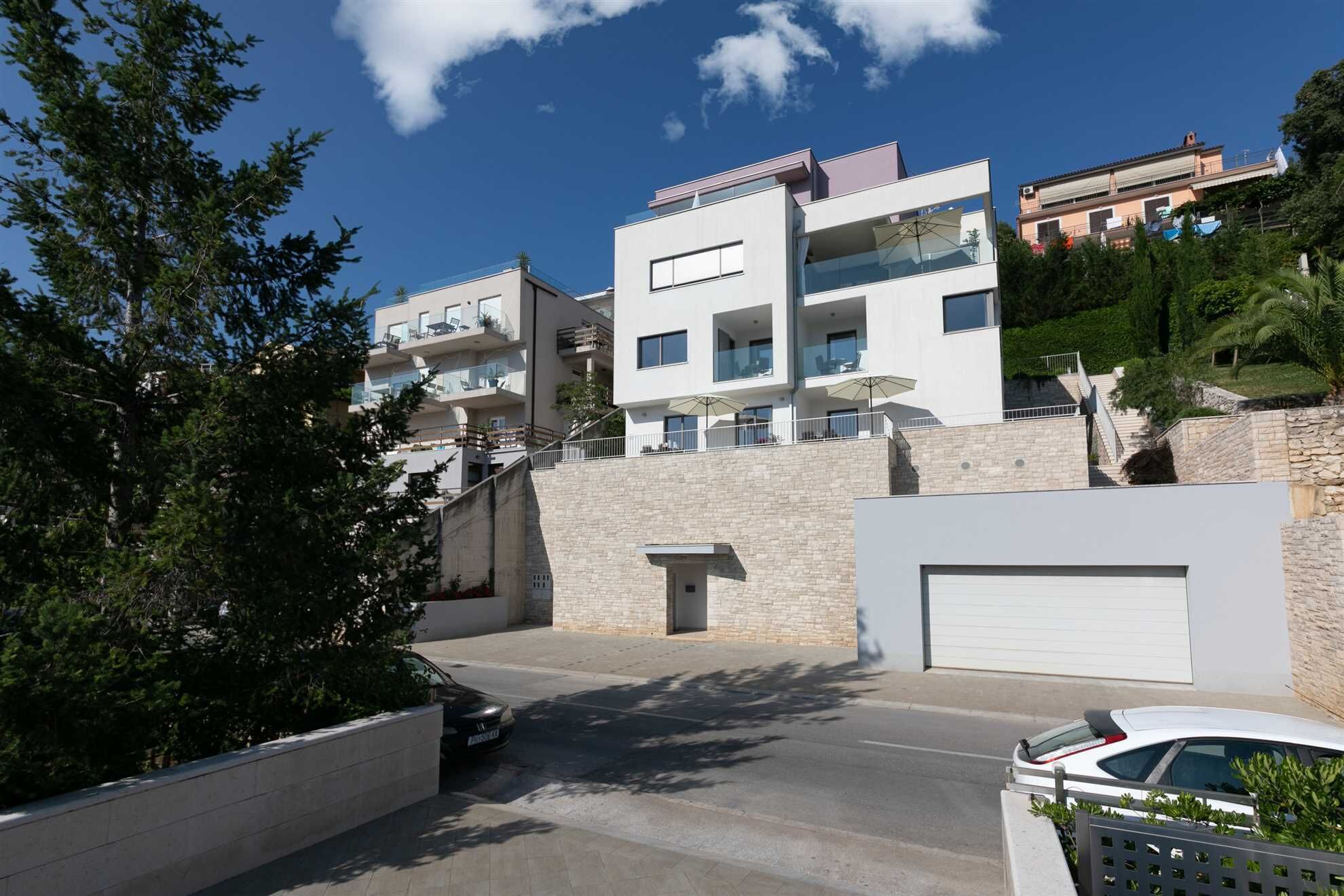 A modern multi-story residential building with balconies, a stone facade, and a garage.