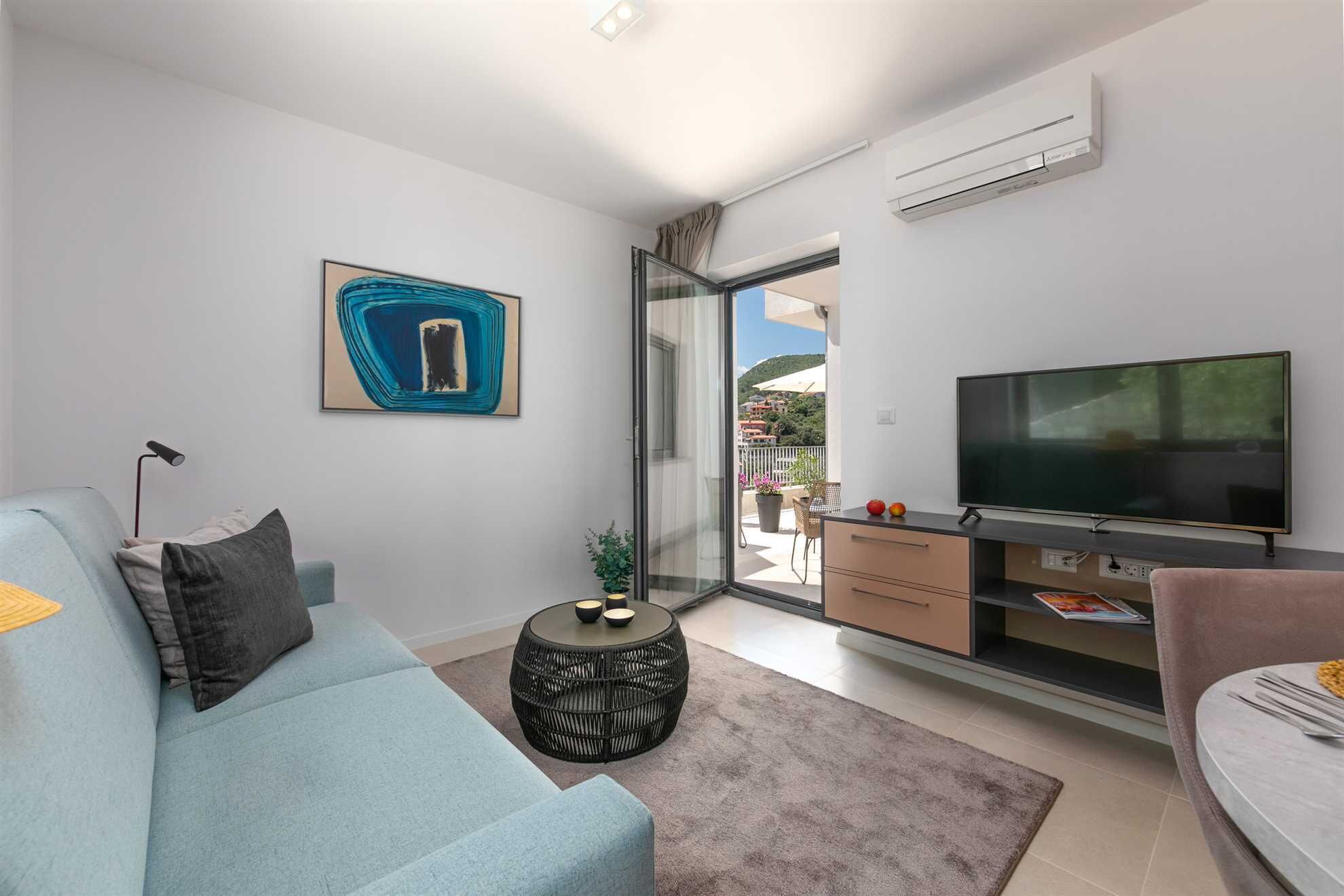 A modern living room with a sofa, a TV, a small side table, and a balcony with a view.