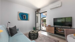 Ein modernes Wohnzimmer mit einer Couch, einem Fernseher, einem kleinen Beistelltisch und einem Balkon mit Blick.