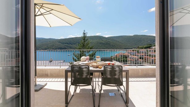 Un balcone con un tavolo apparecchiato per due, con vista su un lago e delle colline.