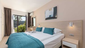 Camera d'albergo moderna con un letto grande, comodini, un tavolino da notte, un quadro e vista sul verde.