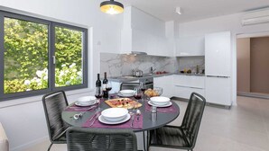 Una cucina moderna con mobili bianchi, una parete di fondo in marmo e un'area pranzo con tavolo rotondo apparecchiata per quattro persone.