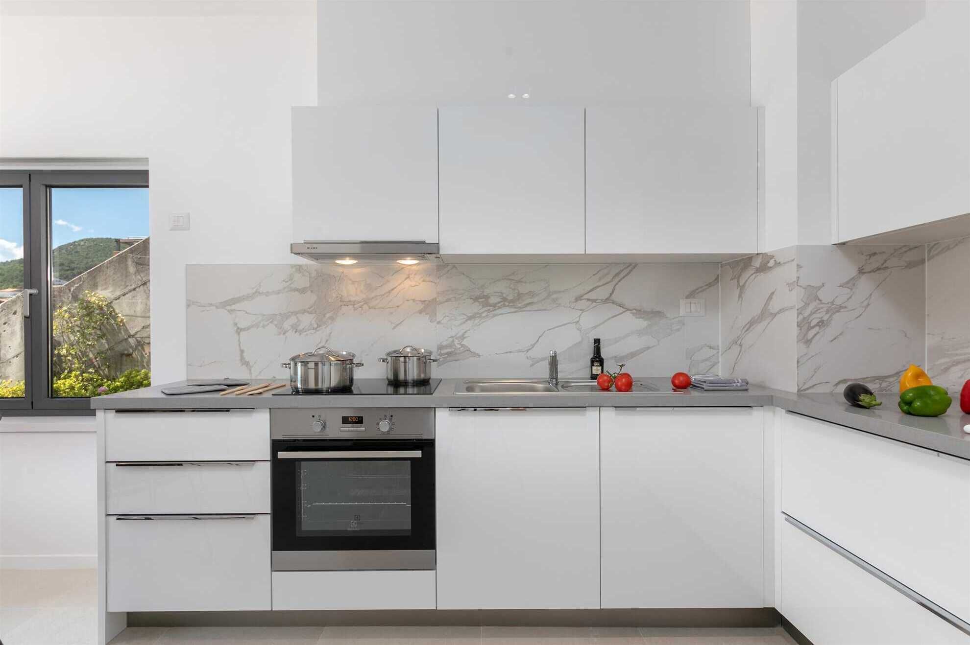 A modern kitchen with white cabinetry, a built-in oven, and a marble backsplash.