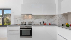 Una cucina moderna con mobili bianchi, forno integrato e piano di lavoro in marmo.