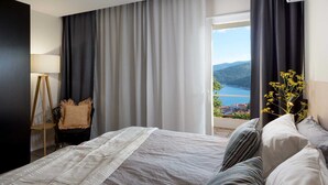 Une chambre d’hôtel moderne avec un grand lit, une vue sur la mer et un balcon agrémenté de fleurs.