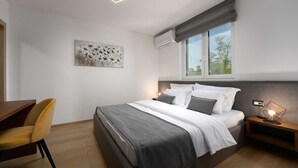 Een moderne slaapkamer met een bed, nachtkastje, stoel, kunstwerk en een raam met uitzicht.