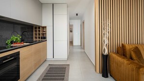 Een moderne keuken met een zwart aanrecht, houten kastjes en een ingebouwde oven. Op het aanrecht staat een klein plantje en er is een zwarte stoel in de eethoek.