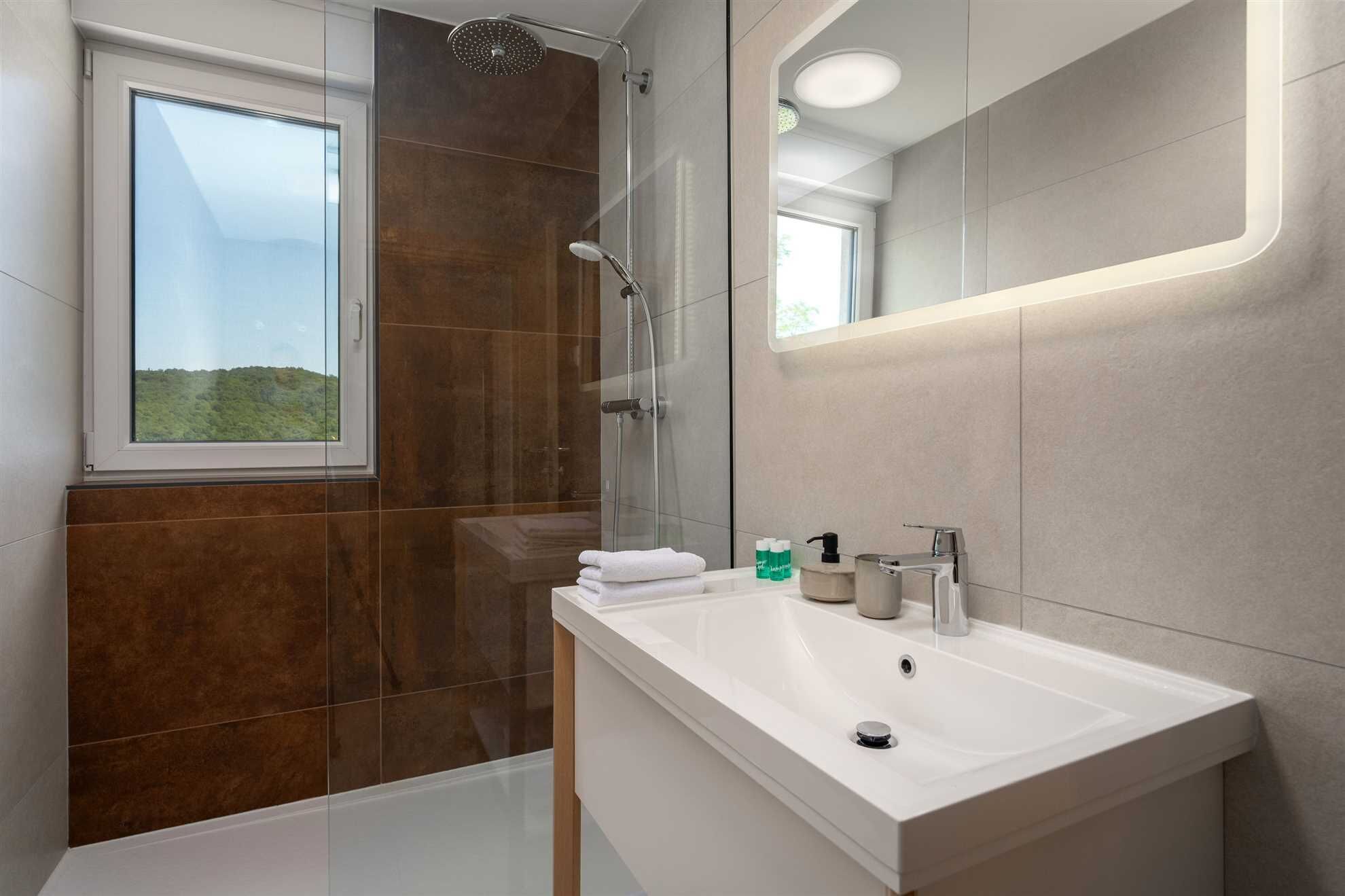 A modern bathroom with a shower, a sink, and a window.