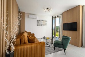 Relax in a spacious living room with a large window offering a view of the outdoors, a flat-screen TV, and a comfortable seating area.