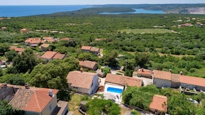 A coastal village with terracotta-roofed houses, a central swimming pool, and a view of the sea and a large bay. - Casa Dorella in peaceful location with a sea view (Viškovići)