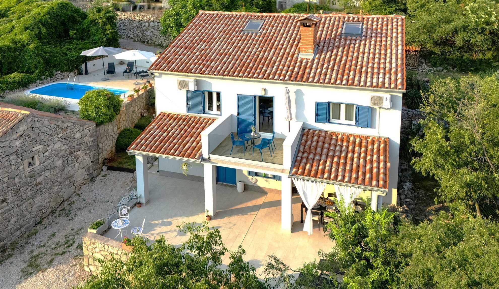 Une maison à deux étages avec une piscine, un espace salon extérieur et un mur en pierre.