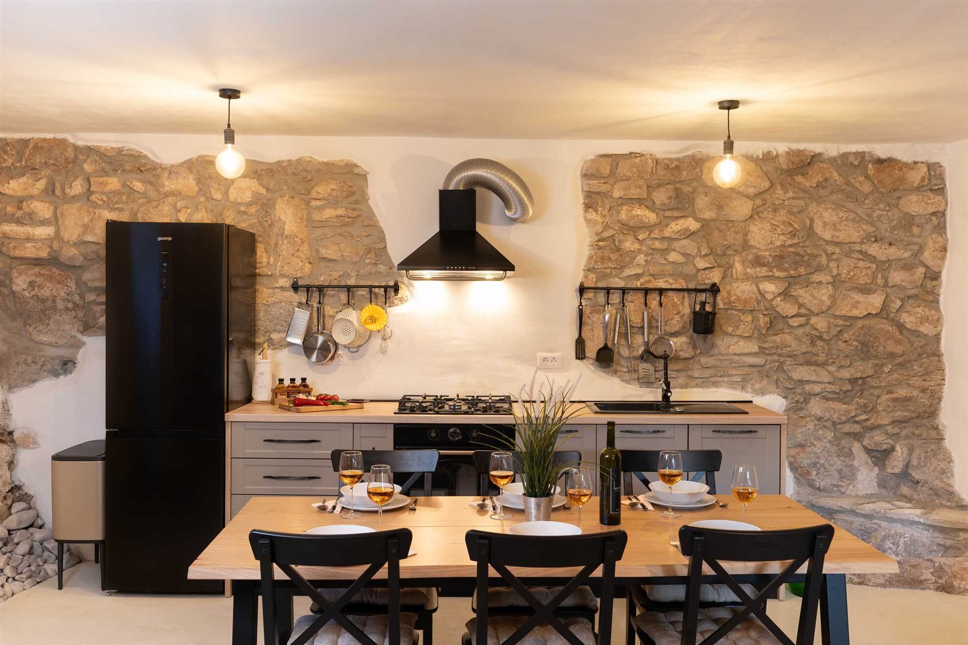 A modern kitchen with stone walls, a black range hood, and pendant lighting.