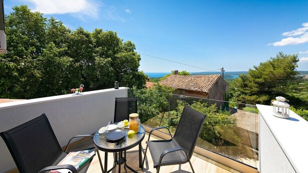 A balcony with a table set for two, a chair, and a view of a rural landscape with a house and trees. - Casa Dorella in peaceful location with a sea view (Viškovići)