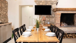 A dining area with a wooden table set for four, surrounded by black chairs. A stone wall and a fireplace are visible in the background. - Casa Dorella in peaceful location with a sea view (Viškovići)