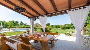 A covered outdoor dining area with a pool and garden view. - Casa Ivanovac with pool and large front yard (Rogočana)