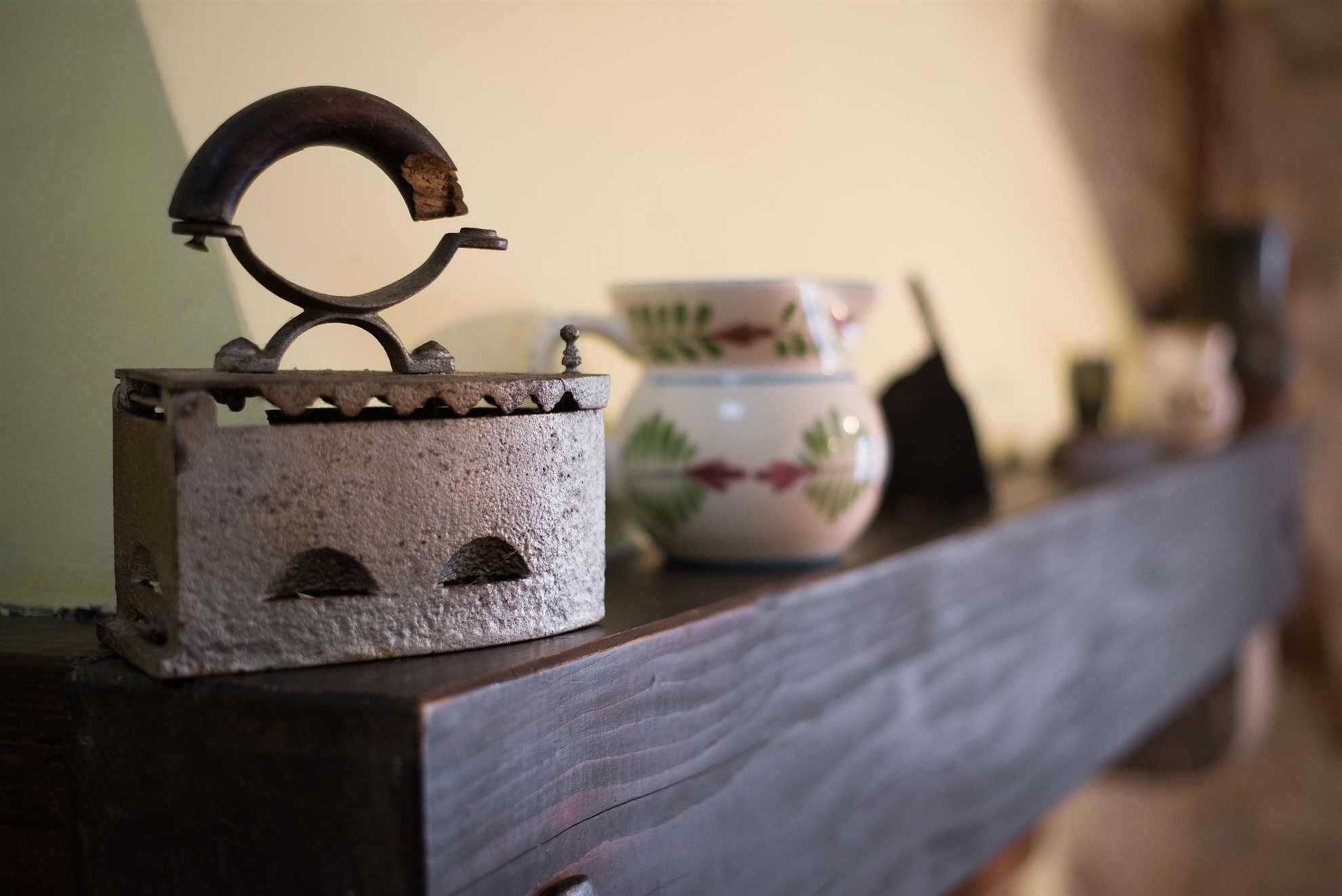 A rustic metal kettle with a handle on a wooden shelf.