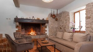 A cozy living room with a fireplace, stone walls, a sofa, and a coffee table. - Casa Ivanovac with pool and large front yard (Rogočana)