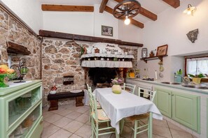 Una cocina rústica con pared de piedra, vigas de madera, chimenea y zona de comedor con mesa y sillas.