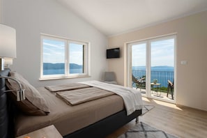 Quarto com cama, televisão e varanda com vista para o mar.