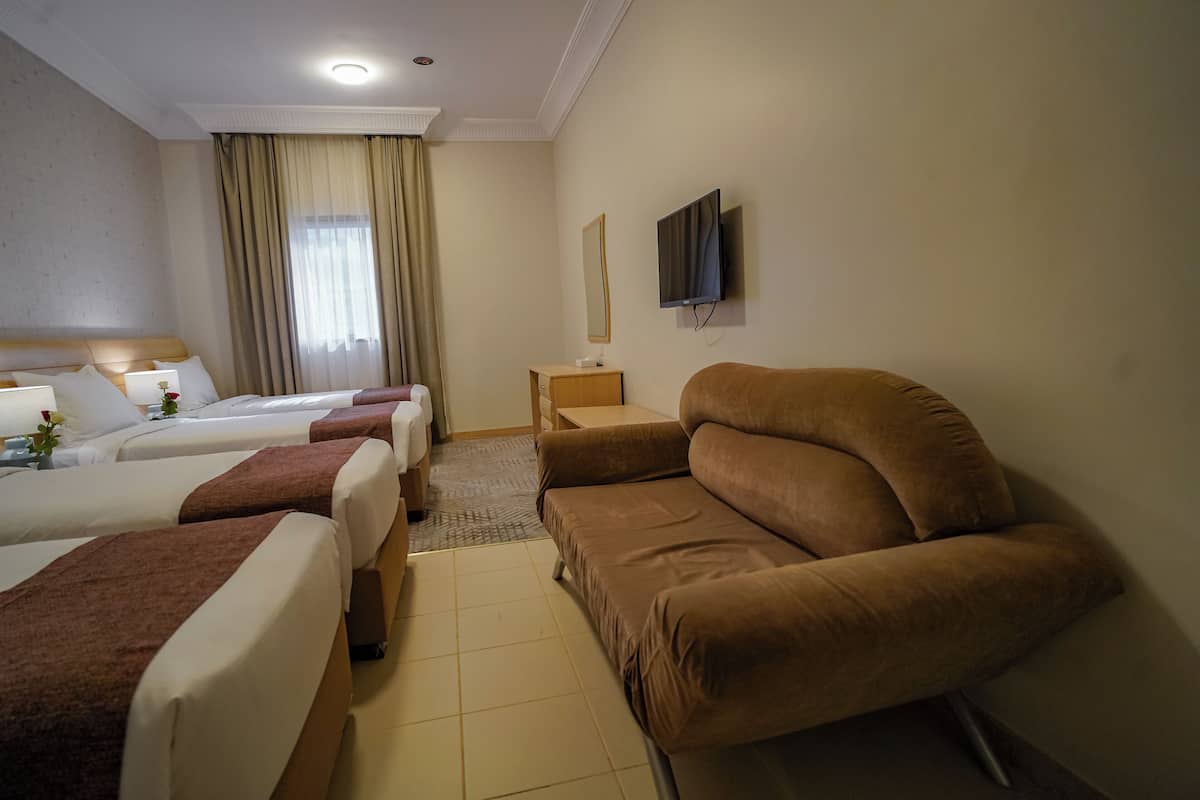 Hotellihuone, jossa on kolme sänkyä, sohva, televisio ja peili.
