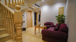 A living room with a staircase, a sofa, a table, and a potted plant. - EMMAR AL NOOR (Makkah)