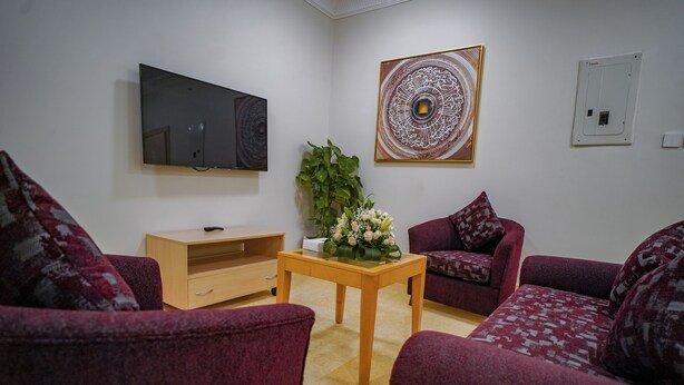 A living room with a TV, a decorative wall piece, a plant, and two patterned sofas. - EMMAR AL NOOR (Makkah)
