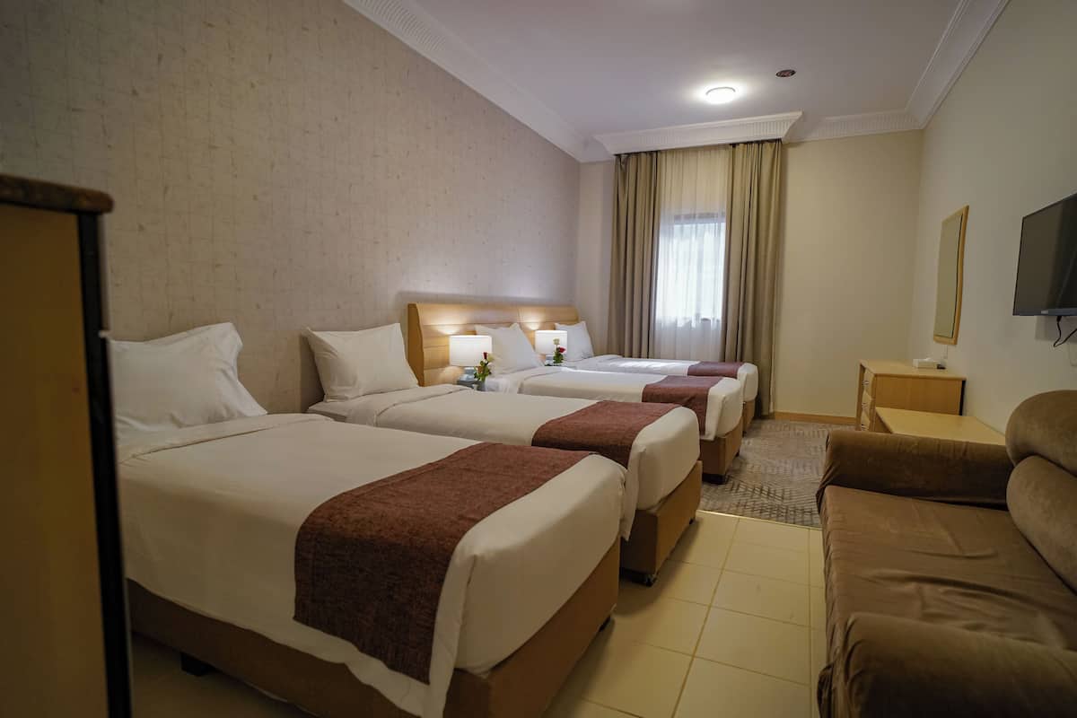 Hotellihuone, jossa on kolme sänkyä, sohva, televisio ja pieni pöytä.