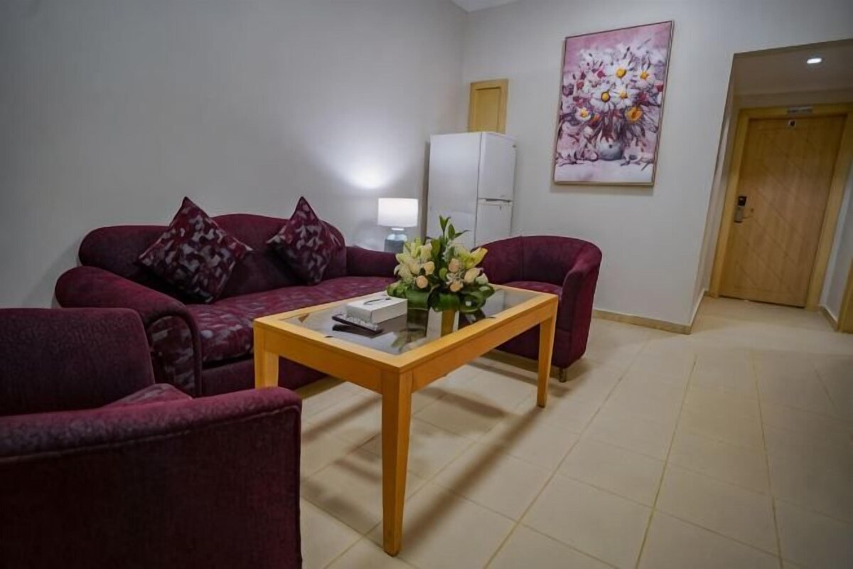 A living room with a sofa, armchairs, a coffee table, a white refrigerator, and a door.