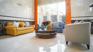 A modern lobby with a marble floor, a round coffee table with a vase of flowers, and two sofas in yellow and blue. - EMMAR AL NOOR (Makkah)