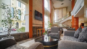 A spacious lobby with comfortable seating, a fireplace, and a large window offering a view of the street. - EMMAR AL NOOR (Makkah)