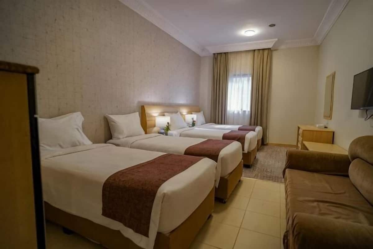 Hotellihuone, jossa on kolme sänkyä, sohva, televisio ja ikkuna, jossa on verhot.