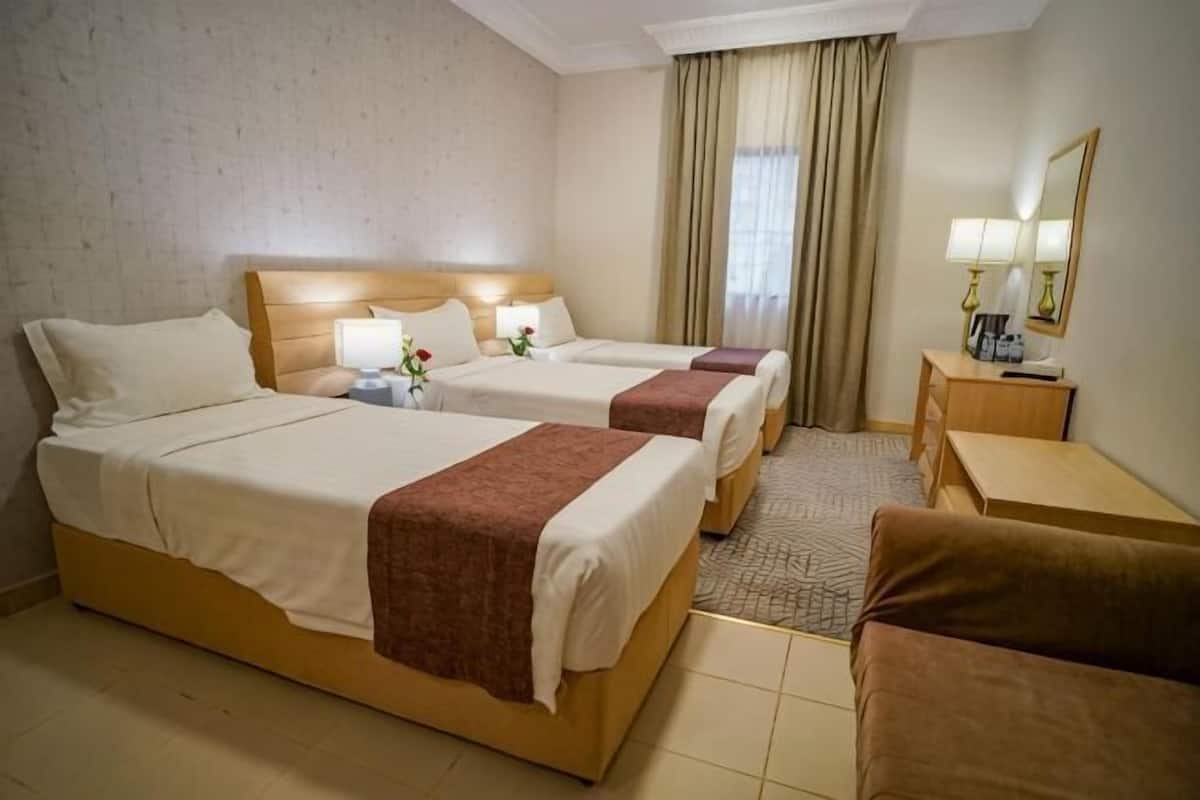 Hotellihuone, jossa on kaksi sänkyä, työpöytä, tuoli, pieni pöytä, peili ja ikkuna, jossa on verhot.
