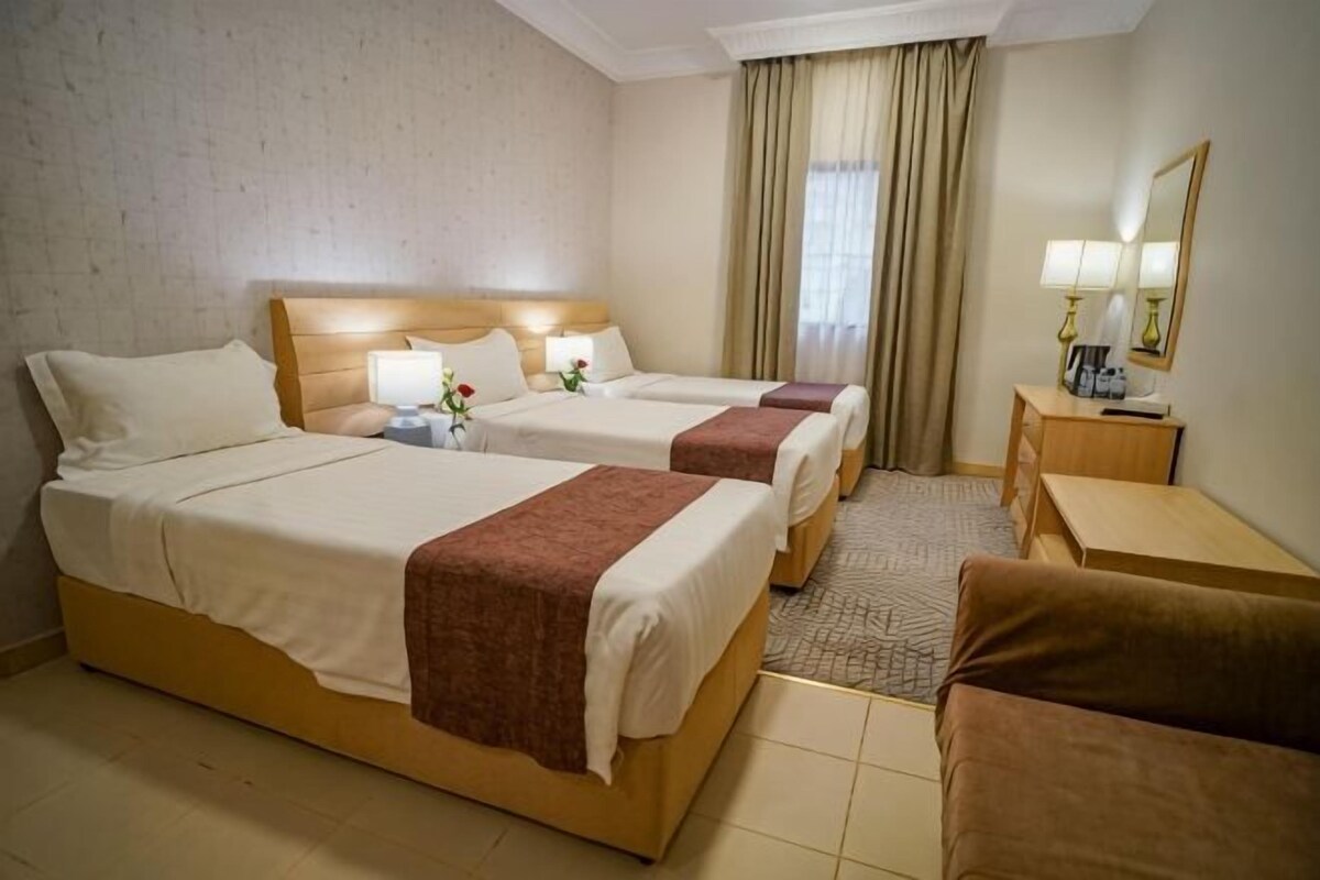 A hotel room with two beds, a desk, a chair, a small table, a mirror, and a window with curtains.