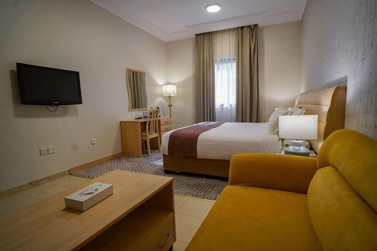 A hotel room with a bed, a desk, a chair, a television, and a window with curtains.