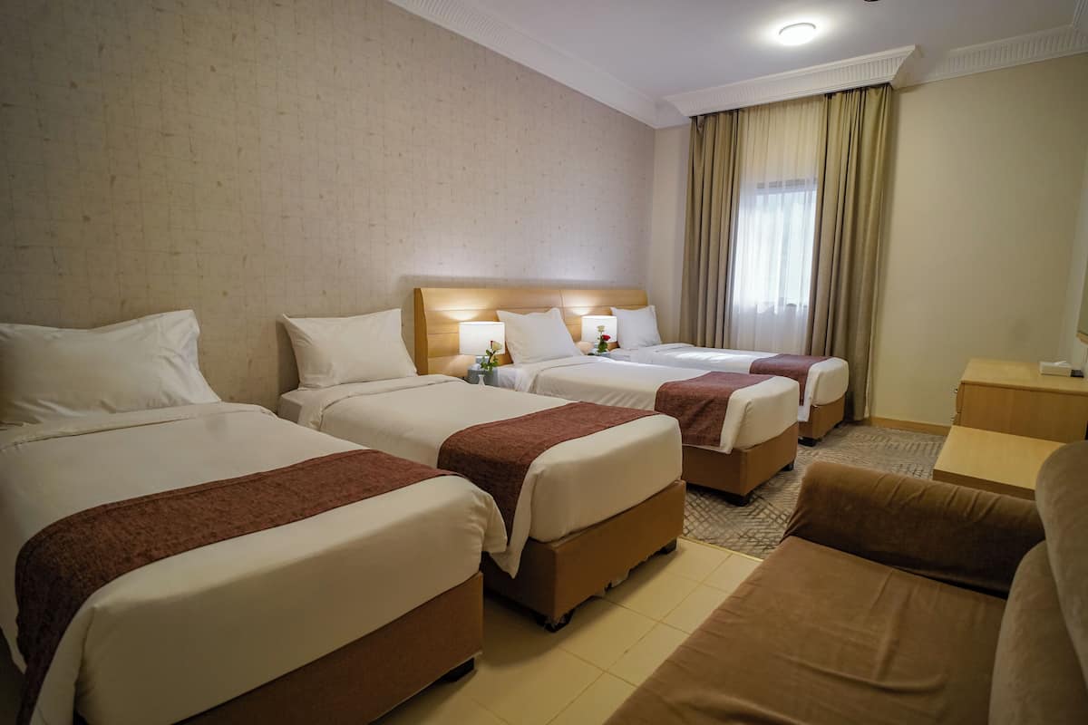 Hotellihuone, jossa on kolme sänkyä, sohva ja työpöytä.