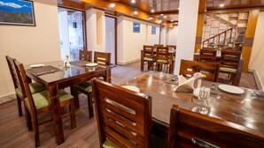 A dining area with wooden tables and chairs, a staircase in the background, and a mountain view on the wall. - Muscatel Stardust - Chowrasta Mall Road (Darjeeling)