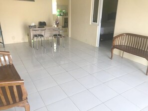 A spacious living area with a tiled floor, a dining table with four chairs, a wooden bench, and a doorway leading to another room. - SPOT ON 93020 Rumah Singgah Ganjuran (Sumbermulyo)