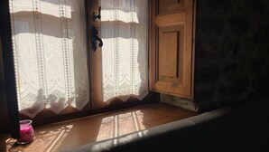 A window with lace curtains, a wooden door, and a candle on a wooden ledge. - Casa El Collau (Sevares)