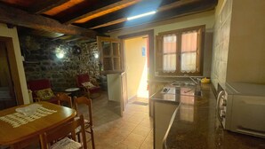 A cozy kitchen with a stone wall, wooden furniture, and a tiled floor. - Casa El Collau (Sevares)