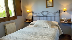 A bedroom with a bed, two bedside tables, a radiator, and two wall-mounted lamps.